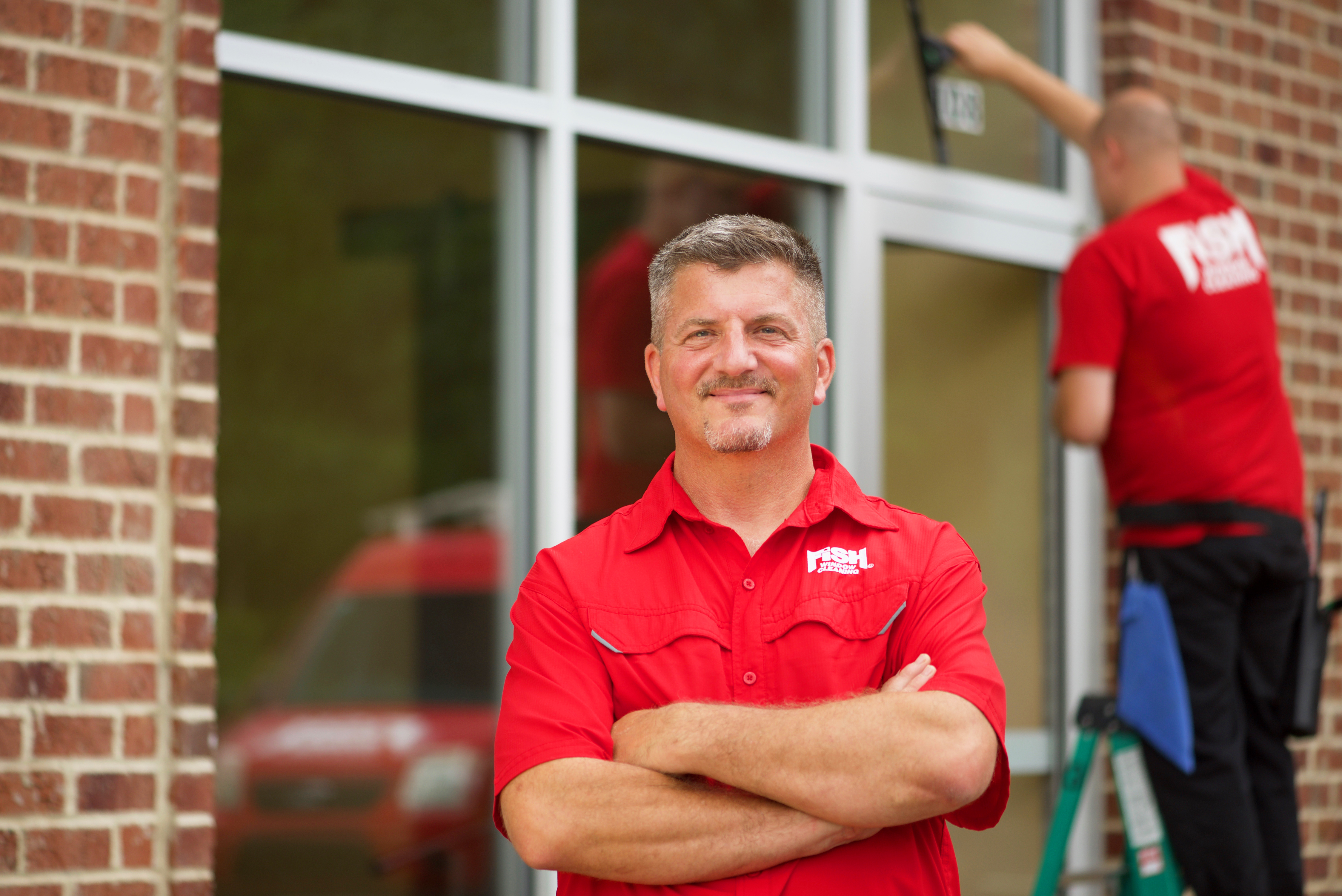 Fish Window Cleaning Franchise Owner with Cleaner Cleaning Windows in Background